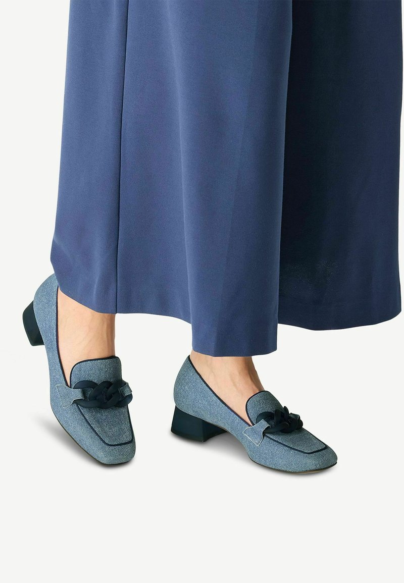 Mocassini con tacco blu dal finish texturizzato, con un accento nero annodato e punta rotonda. Abbinati a un capo fluido blu.