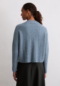 Himmelblauer, kabelgestrickter Pullover mit cropped Design, weicher Textur und langen Ärmeln, kombiniert mit einem dunklen Rock.