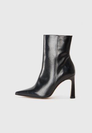 Stivale alla caviglia in pelle nera con punta affusolata e tacco a stiletto. Presenta una texture liscia e un design minimalista con una silhouette elegante.