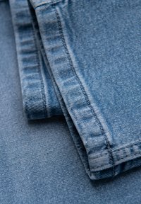 Tissu en denim bleu clair, montrant un gros plan des bords pliés, avec des coutures visibles et de légères variations de texture.