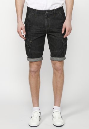 Pantalones cortos de cargo de mezclilla oscura con puños enrollados, que presentan bolsillos laterales, costuras amarillas y un cierre de botón en la cintura.