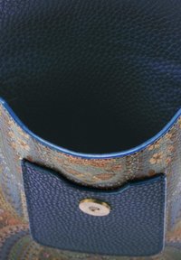 Opengewerkt stoffen tasje met een donkere, textuurrijke leren binnenkant en een buitenzak van leer, die wordt afgesloten door een ronde metalen knop.