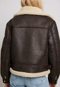 Brun shearlingjakke med et tekstureret læderudvendigt, kremfarvet fleecekrave og justerbare detaljer ved taljen. Casual design.