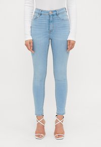 Jeans skinny de culoare albastru deschis, din denim, cu talie înaltă, cusături subtile și asortați cu sandale albe cu curea.