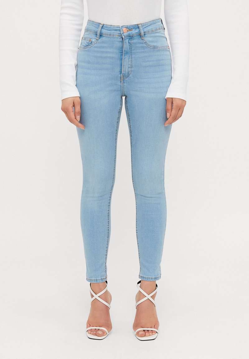Jeans skinny de culoare albastru deschis, din denim, cu talie înaltă, cusături subtile și asortați cu sandale albe cu curea.