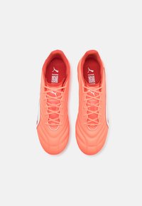 Botte de football corail vif avec une tige synthétique lisse, des panneaux texturés, une marque blanche et des lacets fins. L'intérieur est doté d'un rembourrage rouge.