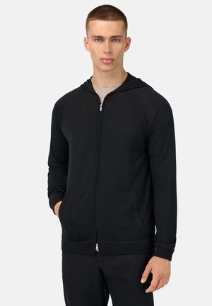 Zwarte rits-hoodie van zachte stof, met een trekkoordhood, voorzakken en ribgebreide manchetten en zoom. Glad textuur, eenvoudig ontwerp.