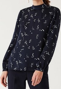 Blusa a maniche lunghe blu navy con motivo floreale bianco su tutta la superficie, colletto alto e polsini arricciati, realizzata in tessuto leggero.