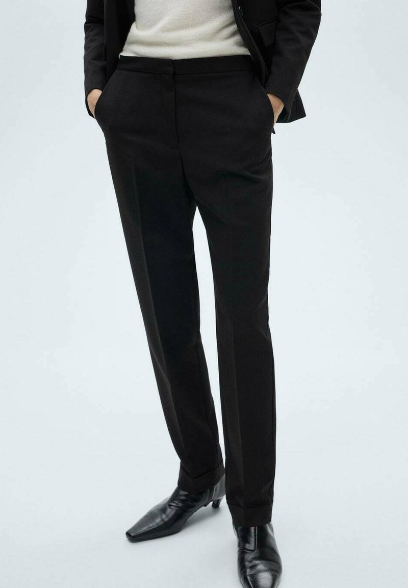 Pantaloni neri su misura con una vestibilità slim, dotati di tasche laterali e una superficie liscia. Abbinati a eleganti scarpe nere.