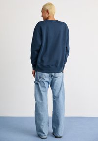 Sweatshirt azul-marinho com um corte descontraído, decote redondo e punhos canelados, combinado com jeans de pernas largas azul-claro com bolsos com pala.