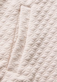 Texturovaná látka v světle béžové barvě s diamantovým vzorem; má jemný pletený materiál s mírně zvýšeným povrchem.