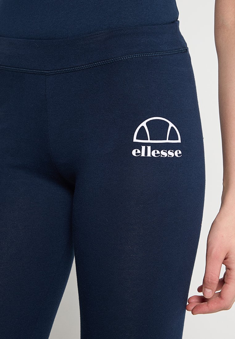 Leggings blu navy con una superficie liscia, dotati di un logo ellesse bianco e un design ad arco sulla coscia sinistra. Vita elasticizzata per il massimo comfort.