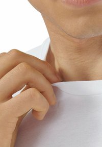 Biała bawełniana koszulka z okrągłym dekoltem. Ręka dostosowuje kołnierzyk. W okolicy dekoltu widoczny jest odcień skóry. Zauważalna jest miękka tekstura.