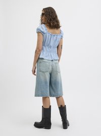 Light blue, puff-sleeve top with smocked waist and ruffled hem, paired with faded denim Bermuda shorts and knee-high black boots.