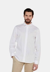 Camicia bianca a maniche lunghe con leggere righe verticali, colletto button-down e taschino sul petto; tessuto liscio, vestibilità sagomata.
