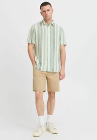 Kortærmet skjorte med knapper i grønne og hvide lodrette striber, parret med beige shorts. Fodtøj: hvide sneakers med snørebånd.