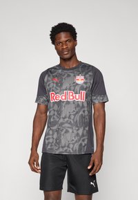 Maillot de sport gris à manches courtes avec un motif texturé, logo Red Bull et marquage Puma, associé à un short noir.