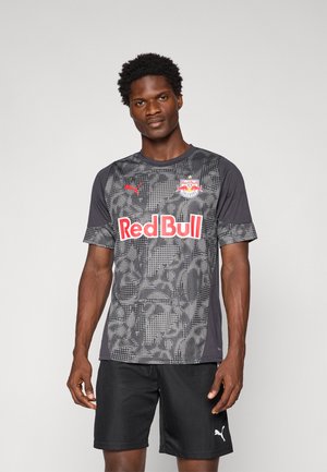 Šedý sportovní dres s krátkým rukávem, který má texturovaný vzor, logo Red Bull a branding Puma, doplněný černými kraťasy.