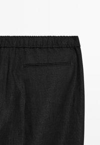 Black linen pants with an elastic waistband, featuring a flat pocket on the back and a textured fabric for a relaxed fit.