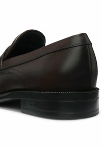 Czarny skórzany elegancki but z niskim obcasem, widocznym przeszyciem i wytłoczonym napisem "BOSS" na zewnętrznej stronie pięty.