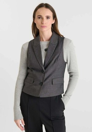 Grijze gestreepte vest met een getailleerd ontwerp, notch revers, twee voorzakken en zwarte knopen, gedragen over een lichtgrijze langemouwen sweater.