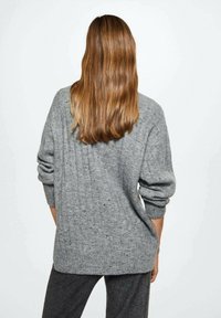 Szary sweter dziany z prążkowaną fakturą, z opuszczonymi ramionami i luźnym krojem. Noszony na ciemnych spodniach, widok z tyłu.