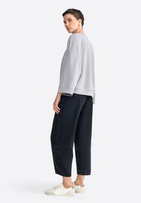 Sudadera oversized de color gris claro con hombros caídos, combinada con jeans de pierna ancha negros y zapatillas blancas con acentos beige.