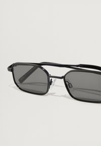 Čierne obdĺžnikové slnečné okuliare s tmavosivými sklami a štíhlym kovovým rámom. Obsahujú textúrované detaily na ramenách a nosných podložkách pre pohodlie.