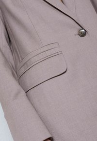 Svetlohnedé sako s výbrusom klopy, zapínaním na jeden gombík a vreckom s dvojitým šitím. Hladká, textúrovaná látka.