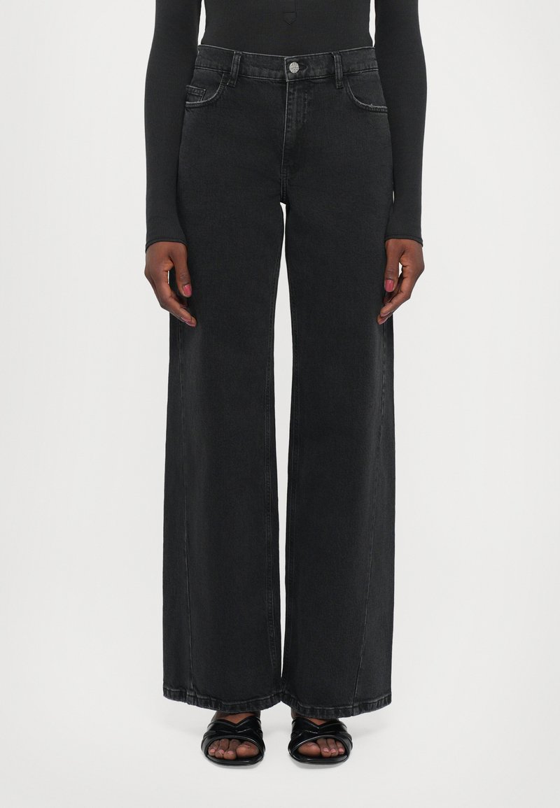 High-waisted black wide-leg jeans made of denim, featuring front pockets, a button closure, and a clean finish. Worn with black sandals.