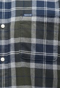 Kék, szürke és zöld kockás anyag, elülső melltartó zsebbel és fehér gombokkal, a zseb szélén kis Barbour márkajeggyel.