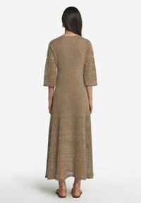 Langes, geripptes, braunes Strickkleid mit Dreiviertelärmeln, das ein Spitzenmuster und einen ausgestellten Saum hat. Kombiniert mit Sandalen mit Riemchen.
