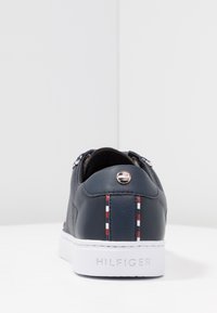 Sneaker in pelle blu navy con suola in gomma bianca, caratterizzata da dettagli a strisce rosse, bianche e blu sul tallone e un logo sul retro.