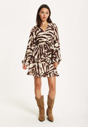 Printed wrap dress with long sleeves, ruffled hem, and a tie belt. Features a brown and cream animal pattern. Paired with brown cowboy boots.