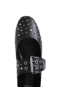 Zapato Mary Jane de cuero negro con remaches circulares plateados, correa ajustable con hebilla y punta redondeada. Textura suave con un acabado brillante.