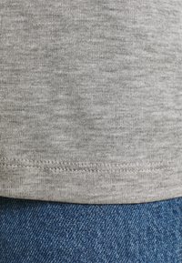 Grijze katoenen T-shirt zoomdetail met een gladde textuur, met een nette afwerking en subtiel gemêleerd patroon, boven blauwe denim.