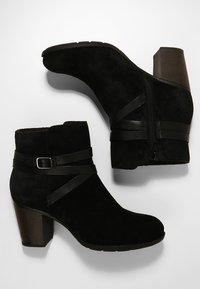 Mustat mokkanahkaiset nilkkurit, joissa on pinoiltu korko, mustat nahkahihnat ja sivussa vetoketju sulkemista varten.