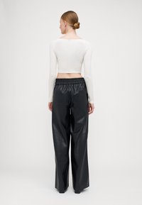 White long-sleeve cropped top paired with black high-waisted, wide-leg pants made of shiny faux leather. Elastic waistband detail.