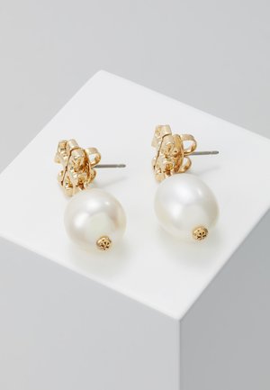 Pendientes de studs en tono dorado que presentan grandes perlas blancas lisas, diseñados con un cierre en forma de flor y detalles de hardware visibles.