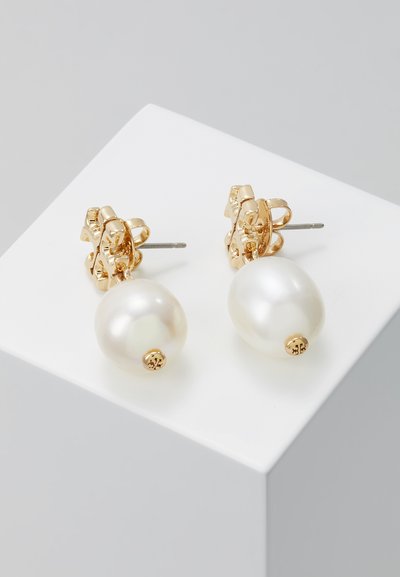 Orecchini a perno color oro dotati di grandi perle bianche lisce, progettati con una chiusura a forma di fiore e dettagli hardware visibili.