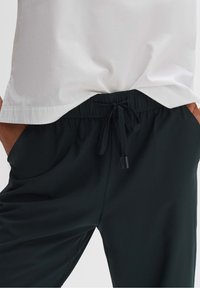 Pantalon noir à cordon de serrage avec une taille élastique, une texture douce et des poches latérales inclinées, associé à une chemise blanche unie.