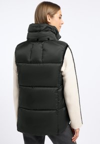 Donkergroene gewatteerde vest met hoge kraag, horizontale stiknaad en zwarte accenten langs de mouwloze armsgaten. Logo gedrukt op de achterkant.