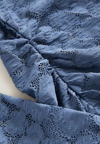Tissu en dentelle bleue avec des motifs floraux et des coutures froncées créant texture et plis.