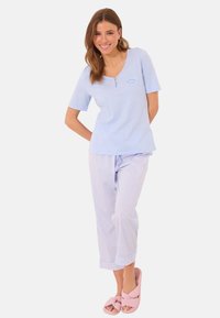 Haut bleu clair à manches courtes avec un col en V et des boutons sur le devant, associé à un pantalon de pyjama rayé bleu clair et blanc. Sandales à glissière roses.