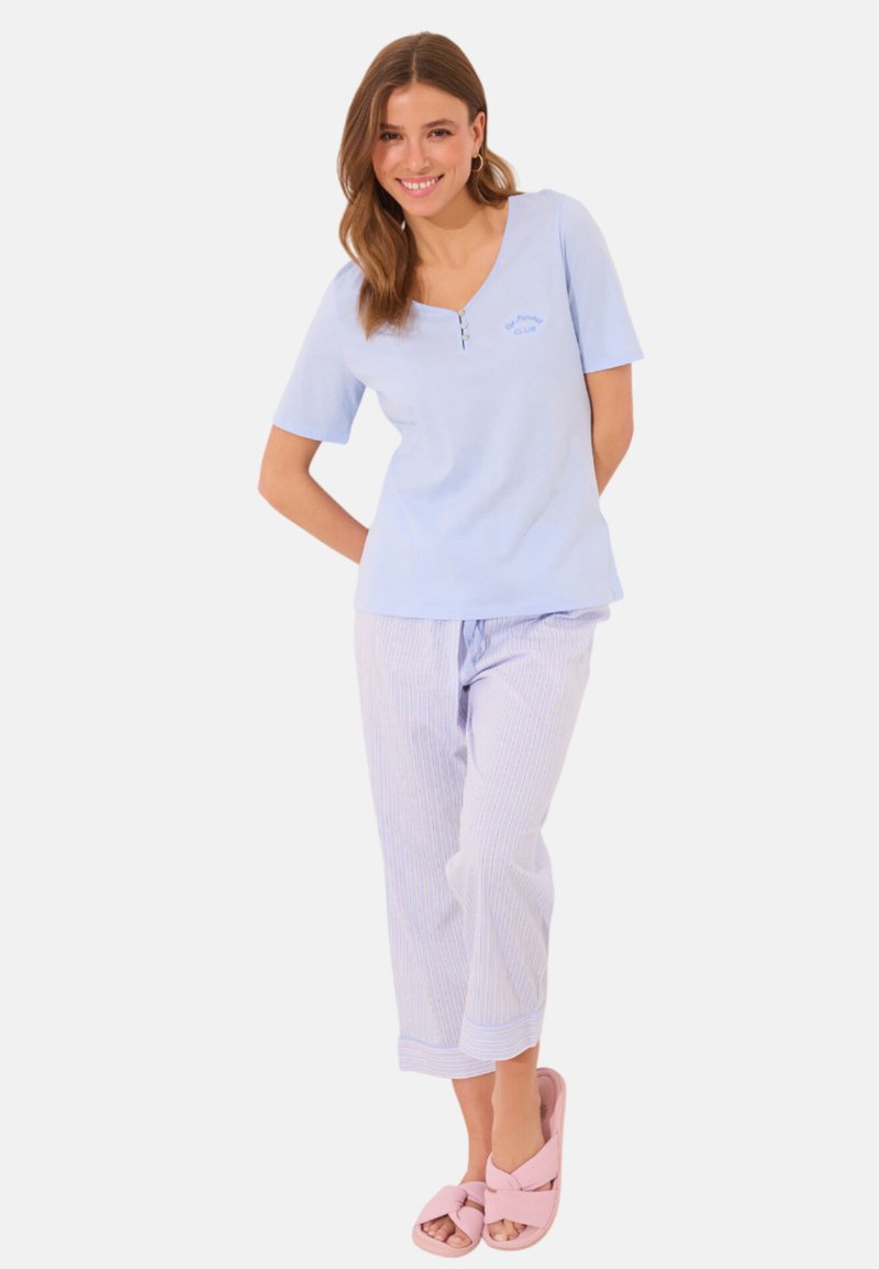Haut bleu clair à manches courtes avec un col en V et des boutons sur le devant, associé à un pantalon de pyjama rayé bleu clair et blanc. Sandales à glissière roses.