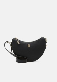 Sac bandoulière en cuir noir en forme de demi-lune, avec une fermeture éclair dorée et un logo, ainsi qu'une sangle réglable. Surface texturée.