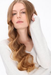 Lichtgrijze geribde trui met een brede halslijn, zachte textuur en verlengde mouwen. Losse golvende haren vallen over de schouder.