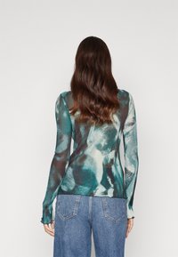 Long-sleeve top with a teal and black abstract pattern, ribbed texture, and flared cuffs paired with blue high-waisted jeans.