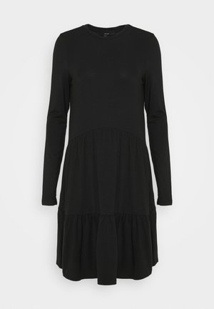 Svart långärmad klänning i mjukt tyg, med rund halsringning och en flerlagers, volangklädd nederkant för extra fyllighet vid fållarna.