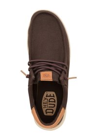 Scarpa in tela marrone con un accento in pelle beige sul tallone, design con punta arrotondata e lacci marroni. Presenta il logo "HEY DUDE" sulla soletta.